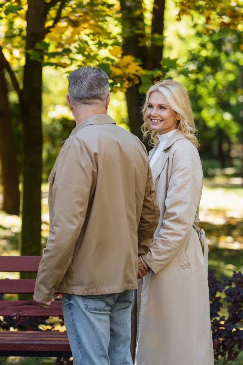 A smiling woman holding hands with a man while walking together in a sunlit park near Livana Fair Lawn in New Jersey.